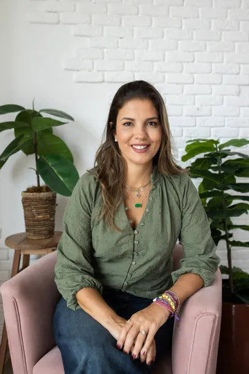 Cristina Senise, psicóloga, sentada em uma poltrona, sorrindo, vestindo blusa verde.